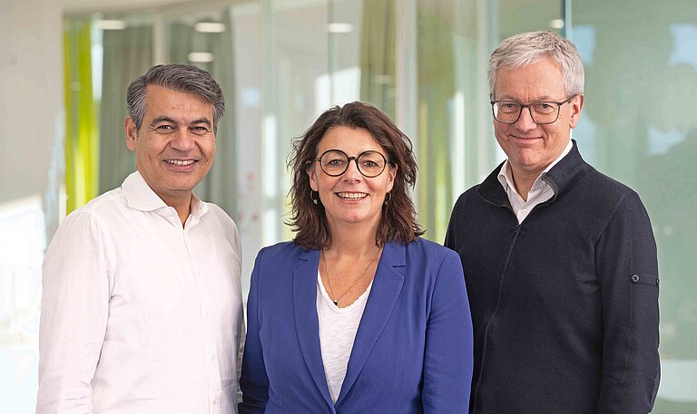 Zwei Männer, eine Frau stehen beisammen und schauen in die Kamera