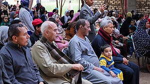 Frauen, Männer und Kinder sitzen bei einer Informationsveranstaltung im Freien in Qena, Ägypten, um über Kinderrechte und Schutzmaßnahmen informiert zu werden.