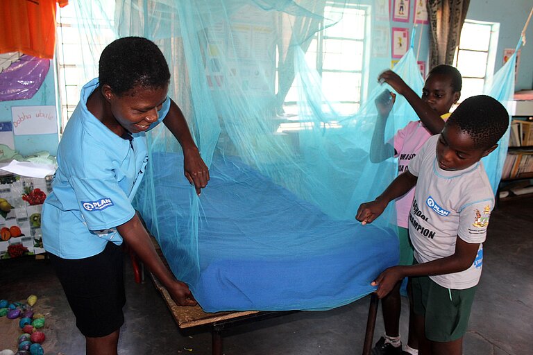 Kinder spannen ein Moskitonetz über ein Bett