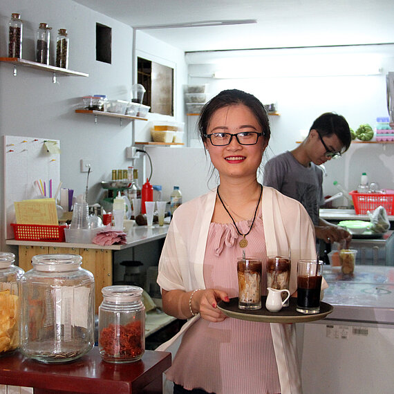 Frau mit Tablett serviert Getränke in einem kleinen Café in Vietnam.
