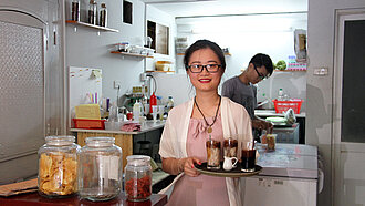 Frau mit Tablett serviert Getränke in einem kleinen Café in Vietnam.