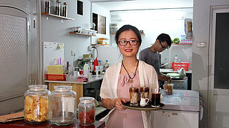 Frau mit Tablett serviert Getränke in einem kleinen Café in Vietnam.