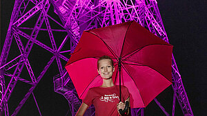 Toni Garrn steht mit einem pinken Regenschirm vor dem pink Funkturm in Berlin.
