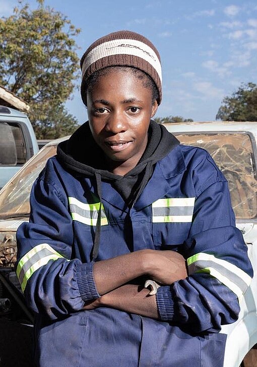 Eine junge Frau steht selbstbewusst an einem Auto und lächelt