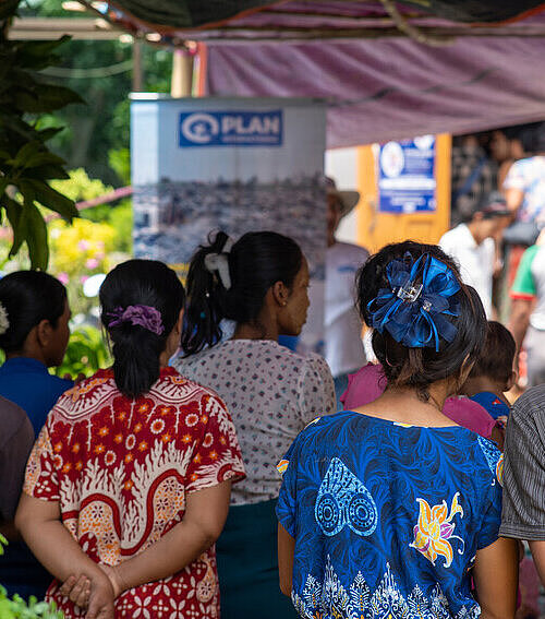 Plan International verteilt Hilfspakete an vom Erdbeben betroffene Familien in Mandalay Eine Gruppe Menschen steht unter einem Planendach und wartet