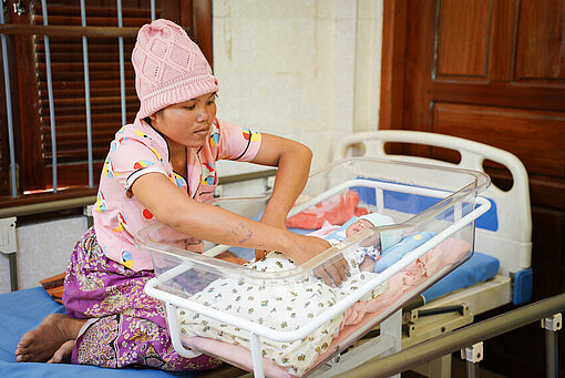 Eine Frau legt ein neugeborenes Baby in ein modernes Bettchen.