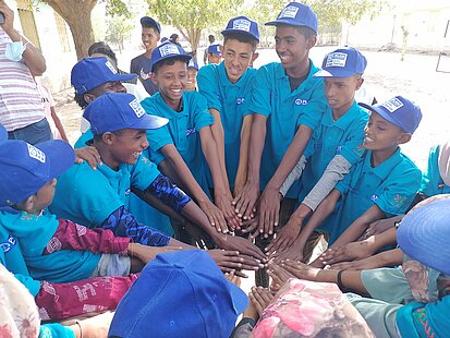 Jungen mit Plan-Kappen stehen im Kreis und legen ihre Hände aufeinander