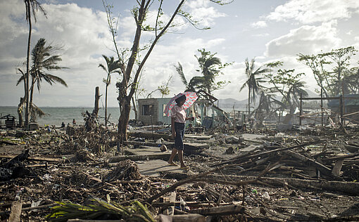 Eine Frau läuft durch ein Trümmerfeld aus Brettern und umgeknickten Bäumen