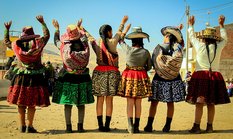Mädchen in traditioneller peruanischer Kleidung stehen in einer Reihe mit dem Rücken zur Kamera