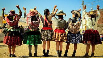 Mädchen in traditioneller peruanischer Kleidung stehen in einer Reihe mit dem Rücken zur Kamera