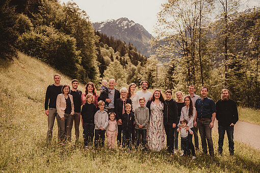 Familie gemeinsam vor einer Berglandschaft bei sonnigem Wetter.