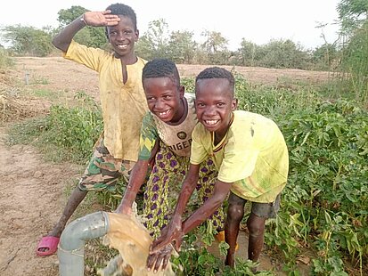 Kinder waschen sich die Hände an einer Wasserstation auf einem Acker