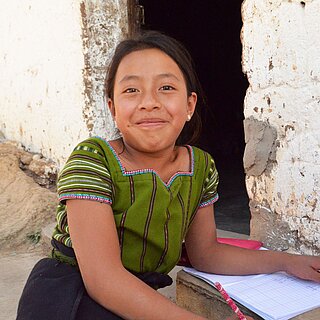 Ein junges Mädchen mit Schulsachen lächelt in die Kamera