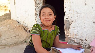 Ein junges Mädchen mit Schulsachen lächelt in die Kamera