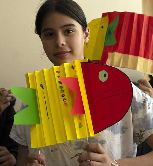 Ein Mädchen zeigt einen bunten Fisch aus Papier, den sie gebastelt hat
