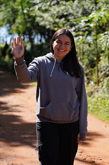 Eine junge Frau steht auf einem Feldweg aus roter Tonerde und winkt
