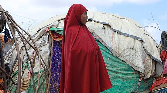 Eine junge Frau aus Somali steht in einem Geflüchtetencamp neben einer Hütte