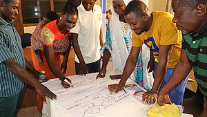 Gruppe von Frauen und Männern arbeitet gemeinsam an einem Flipchart während einer Schulung von Plan International.