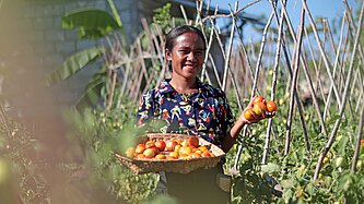Eine junge Frau steht selbstbewusst auf ihrem Feld zwischen Pflanzen