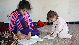Zwei junge Mädchen sitzen auf dem Boden und malen auf Papier