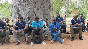 Männergruppe in Afrika sitzt im Kreis unter einem Baum und diskutiert über soziale Themen in der Gemeinde
