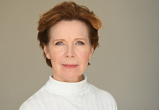 Marion Kracht Eine Frau trägt einen weißen Pullover und hat kurzes Haar
