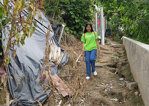 Eine junge Frau mit grünem T-Shirt läuft einen sandigen, steilen Pfad durch Gestrüpp