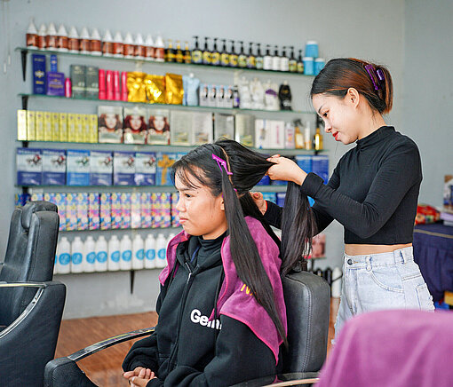 Eine junge Asiatin schneidet einer anderen asiatischen Frau die Haare
