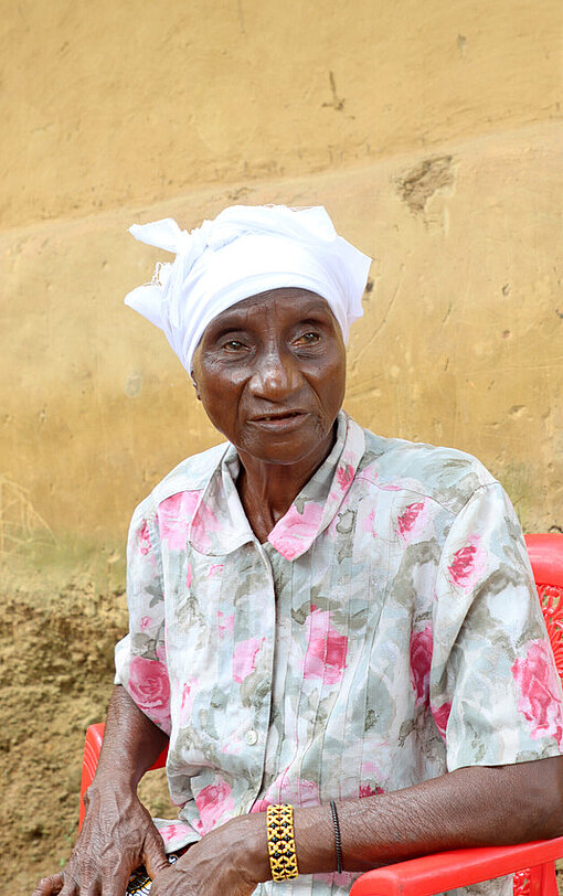 Bendu Hayes sitzt Porträt auf einem roten Gartenstuhl 