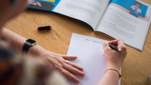 Eine Person sitzt beim Testament schreiben für eine Testamentsspende an Plan International an einem Tisch. Sie schreibt auf ein weißes Blatt Papier.