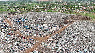 Eine Luftaufnahme zeigt Lastwagen, die vor einen großen Berg von Müll fahren