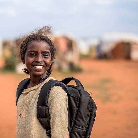 Ein Mädchen mit Schulrucksack lächelt in die Kamera
