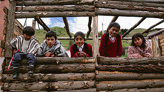 Fünf Kinder lehnen sich über einen Zaun aus Holz