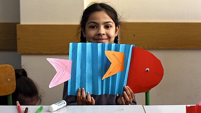 Bild: Ein Mädchen zeigt stolz ihren Papier-Fisch, den sie gebastelt hat.