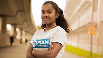 Eine junge Frau mit einem Plan International T-Shirt schaut selbstbewusst in die Kamera.