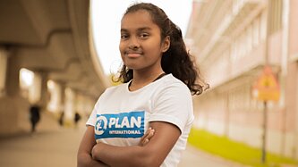 Eine junge Frau mit einem Plan International T-Shirt schaut selbstbewusst in die Kamera.