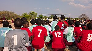 Jugendliche versammeln sich auf dem Fußballplatz in Simbabwe. Jugendliche in roten und türkisfarbenen Trikots sitzen auf einem Fußballplatz in Simbabwe.