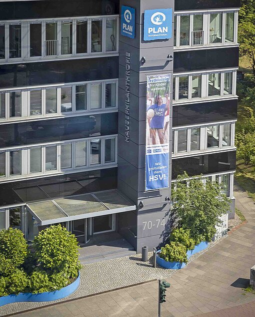 Ein Blick auf ein Bürogebäude, an dem ein Plakat von Plan International hängt