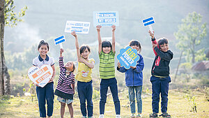 Eine Gruppe von Kindern in Vietnam hält Schilder mit Botschaften wie "I'm helping girls get equal" und "Girl power". Sie stehen auf einer Wiese und zeigen ihre Unterstützung für Geschlechtergleichstellung.