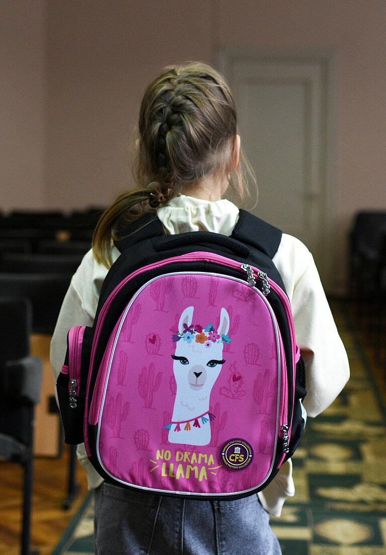 Das Mädchen aus dem Titelbild steht mit dem Rücken zur Kamera. Auf ihrem Lila Rucksack ist ein Lama gedruckt mit der Aufschrift "No Drama Lama"
