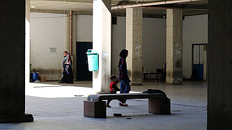 Eine libanesische Jugendliche hat ein Kleinkind an der Hand und läuft mit ihm durch die Notunterkunft