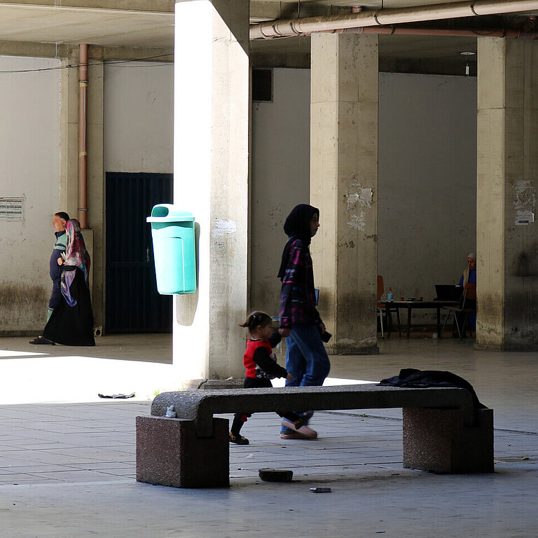 Eine libanesische Jugendliche hat ein Kleinkind an der Hand und läuft mit ihm durch die Notunterkunft