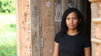 Ein Mädchen lehnt in einem Türrahmen und schaut freundlich aber ernst in die Kamera.