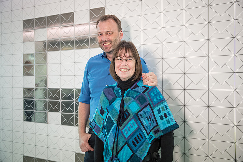 Lächelndes Ehepaar Hollasch vor einer Wand mit "ewigen Briefumschlägen" im Haus der Patenschaften
