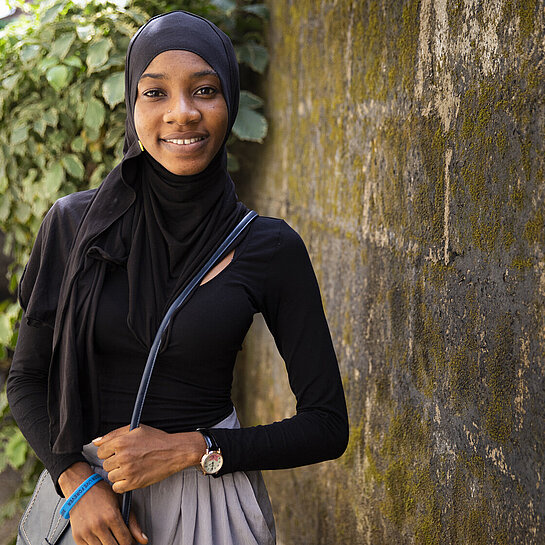 Portrait von Isatu vor einer Mauer und Pflanze.