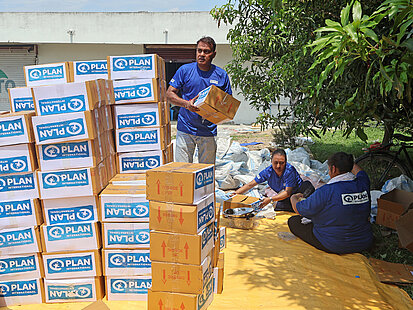 Mitarbeiter von Plan International sortieren und stapeln Nothilfe-Pakete unter freiem Himmel in Nepal zur Versorgung der Betroffenen.