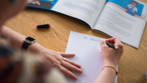 Eine Person sitzt beim Testament schreiben für eine Testamentsspende an Plan International an einem Tisch. Sie schreibt auf ein weißes Blatt Papier.