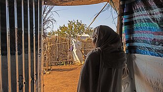 Eine junge Frau blickt aus ihrem Schutzzelt auf einen sandigen Weg