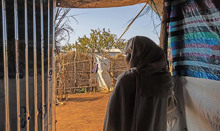 Eine junge Frau blickt aus ihrem Schutzzelt auf einen sandigen Weg