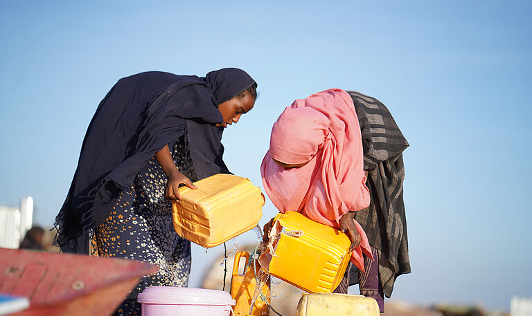Zwei Mädchen holen Wasser aus einem Brunnen.